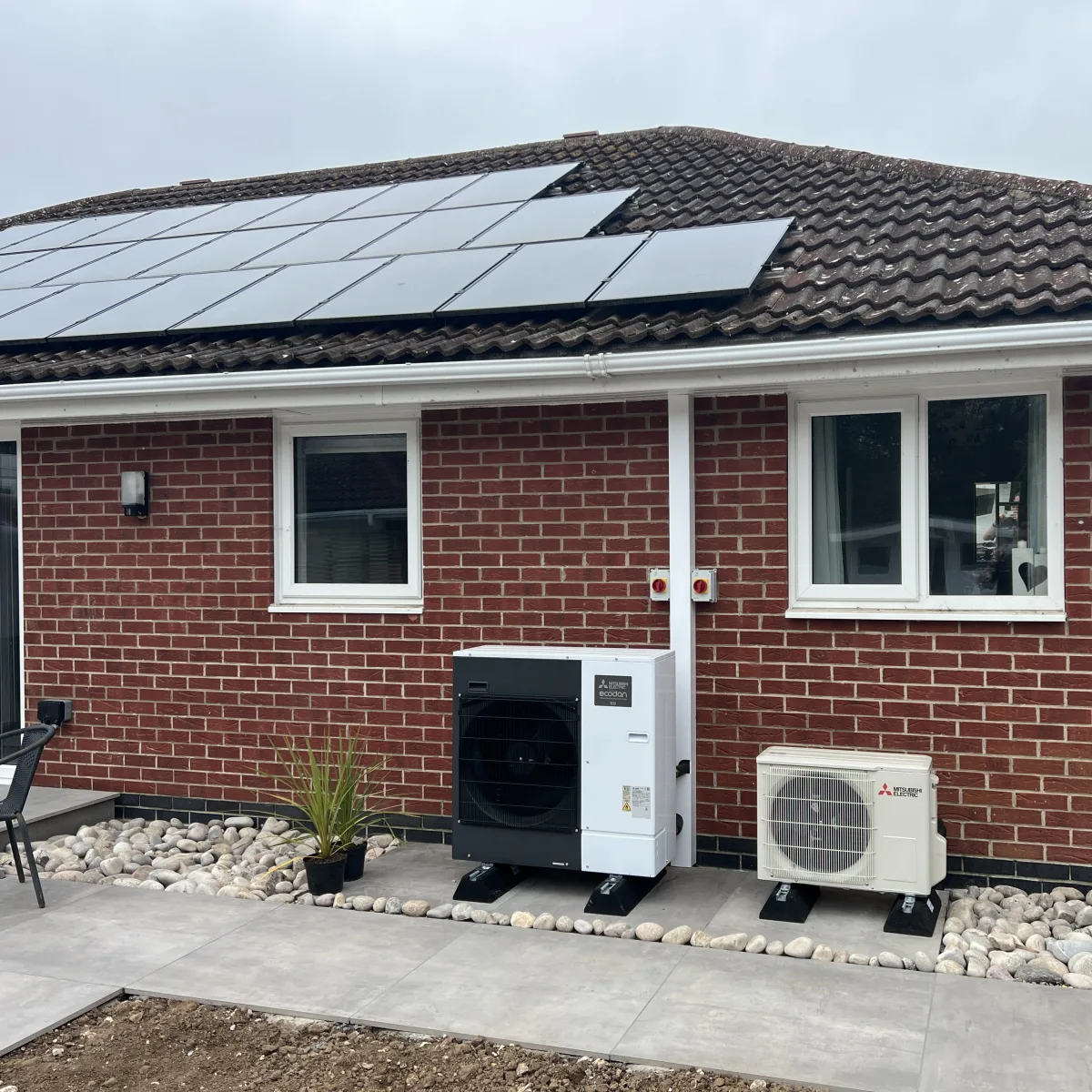 Roof-mounted solar panels above a Mitsubishi Ecodan heat pump and a separate Mitsubishi outdoor unit