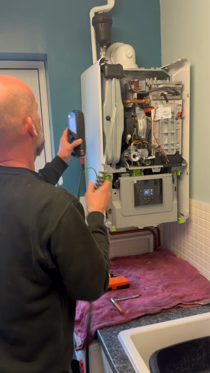 Vector Heat engineer using test equipment while servicing an open gas boiler