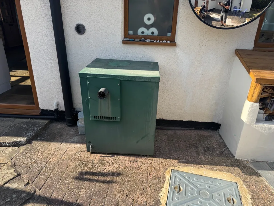 Green outdoor oil boiler installed beside a house
